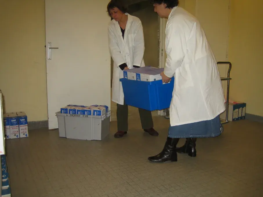 Deux personnes portent une caisse remplie de boîtes d'archives